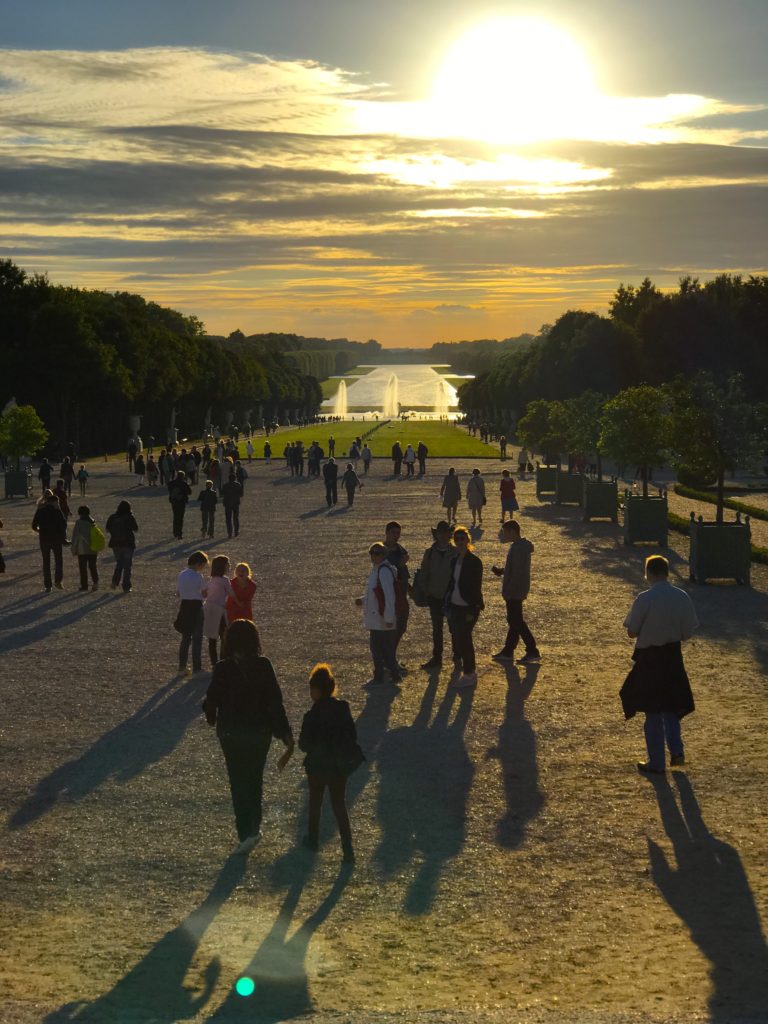 Tourist walking the gardens of versailles at sunset